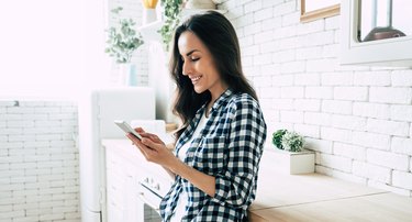 Beautiful cute smiling woman is using smart phone on the kitchen at home.