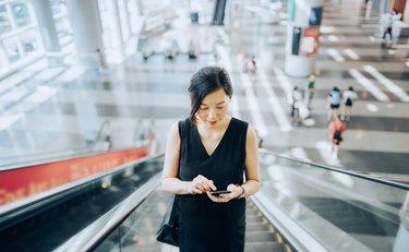 Young businesswoman reading emails on smartphone while riding on escalator