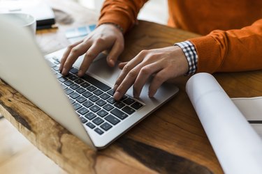 Close-up of man using laptop next to construction plan at desk