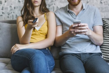 Couple sitting on couch with remote control and smartphone, partial view