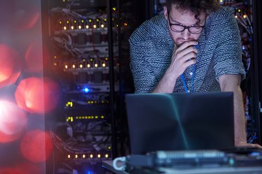 Focused male IT technician working at laptop in dark server room