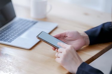 Female hand using smartphone with blank screen at office.