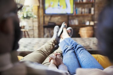 Affectionate couple holding hands, watching TV in living room