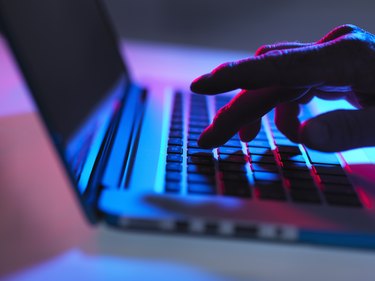 Silhouette of male hand typing on laptop keyboard at night