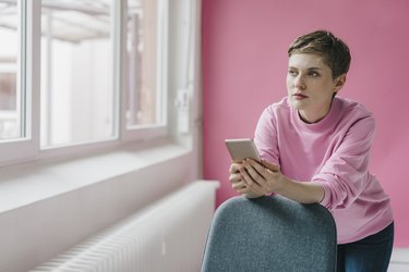 Pensive woman with cell phone looking out of window