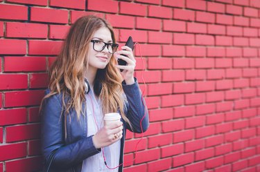 Woman standing next to brick wall with favorite coffee and using mobile phone.