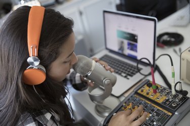 Teenage girl with headphones singing, recording music at microphone equipment