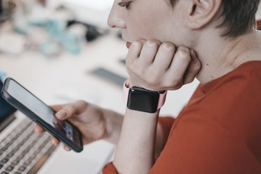Woman wearing smartwatch using cell phone at desk in office