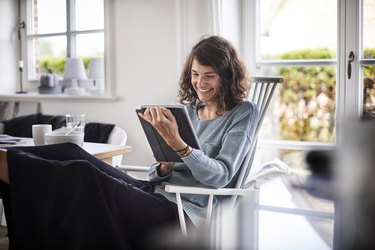 Relaxed young woman sitting at table using tablet