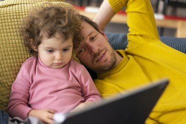 Father and daughter lying on couch watching movie on theit tablet