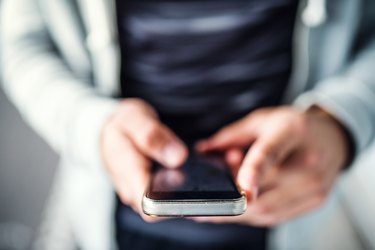 A close-up of unrecognizable young sporty man with smartphone standing in the city.