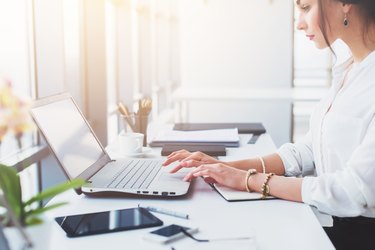 Attractive female assistant working, typing, using portable computer, concentrated, looking at the monitor. Office worker reading business e-mail.