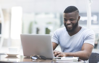 Smiling african man textmessaging on laptop in cafe