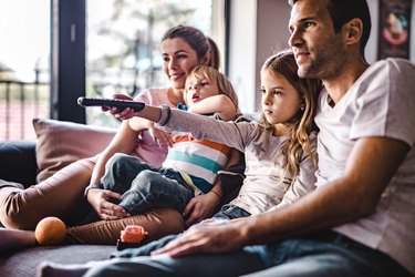 Young parents enjoying with their small kids on sofa while watching TV together.