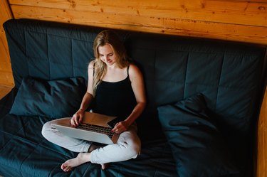 Young business woman sitting on sofa at home and works with a laptop. Girl look and hold Smartphone. Student learning online. Blogger. Side top view of a Computer.