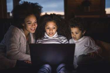 Smiling African American mother and her kids using laptop on sofa at home.