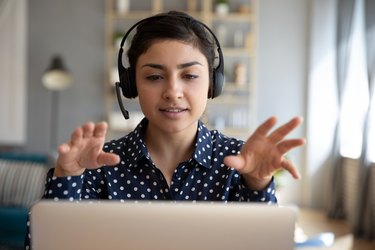 Indian woman teacher wear wireless headset video calling on laptop