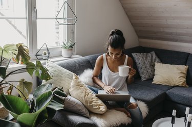 Young woman sitting on the couch with cup of coffee using laptop