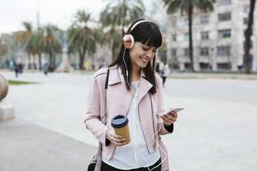 Spain, Barcelona, smiling woman with coffee, cell phone and headphones in the city