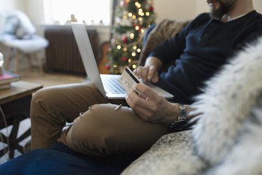 Young man with credit card online Christmas shopping on laptop
