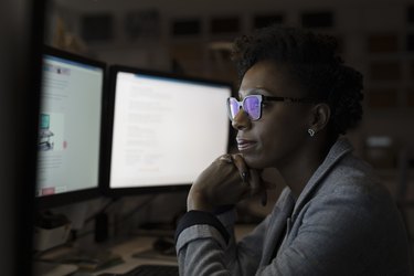 Focused, dedicated businesswoman working late at computers in dark office