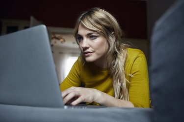 Portrait of woman lying on the couch at home using laptop