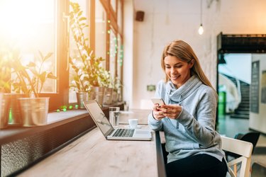 Woman using smartphone and laptop at a lovely bright cafe.