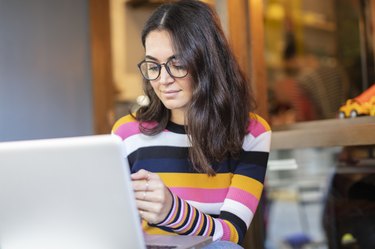 Beautiful Woman with Long Black Hair and Glasses Using a Laptop and Looking to Mobile Phone