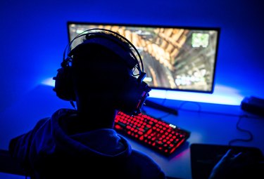 Rear View Of Boy Playing Video Game On Computer In Darkroom