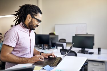 Side view of businessman with dreadlocks using laptop computer on desk in office