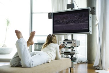 Female lying on chaise longue, watching flat screen television with surround sound