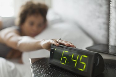 Woman reaching for snooze button on alarm clock.