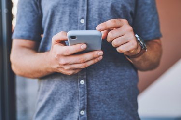 Closeup of man hands on a phone browsing on social media while standing outdoors in the city street. Guy reading an article or blog on a website with a smartphone in an urban town road.