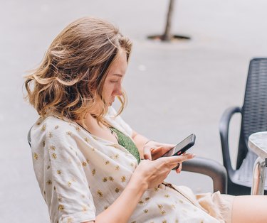 Top view of blonde girl sitting at table using cell phone, Side view of cute Caucasian girl sitting at table outdoors texting on her smartphone