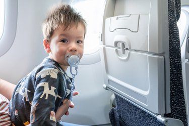 Baby traveling in airplane flying sitting on his mother lap and using pacifier in the aircraft