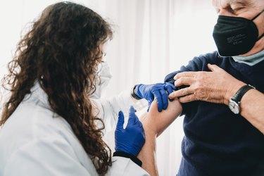 A female doctor is vaccinating a senior man against Covid-19 Coronavirus