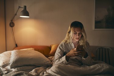Transgender person using mobile phone sitting on bed at home