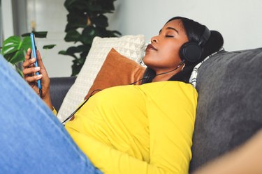 Shot of a young woman wearing headphones and using a cellphone while relaxing on a sofa at home