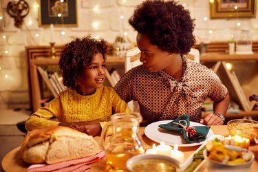 Smiling girl and her mother talking while having Thanksgiving lunch at dining table.