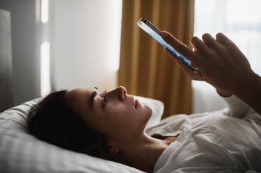 Sad and tired woman lying in bed with phone. Internet and gadget addiction. Melancholy and depression.