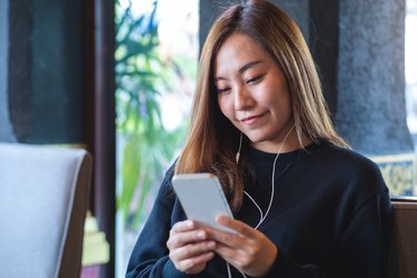 Portrait image of a young woman using mobile phone and earphones to listening to music or online chatting