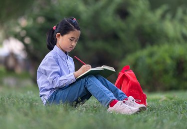 Little Girl Reading and Writing on Grass