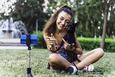 Teenage girl doing a vlog post in the park with her dog.