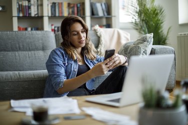 Young smiling woman using mobile phone while studying at home