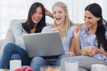 Laughing friends looking at laptop together and eating cookies