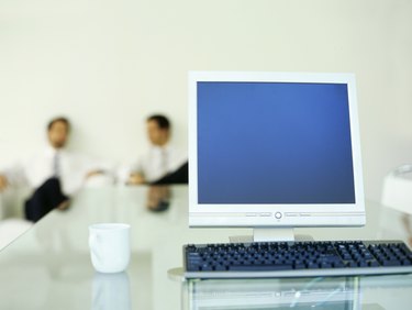 Close-up of a computer with two businessmen sitting in the background