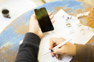 girl writes in notebook, with cell phone and ink drawing