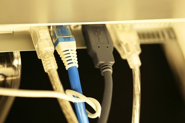 Close-up of ethernet and firewire cables plugged into ports on the back of a laptop computer.