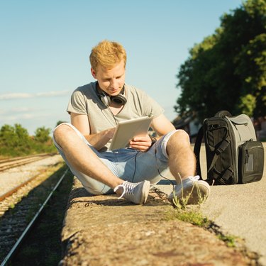 Young hipster man with tablet and headphones outdoors in summer