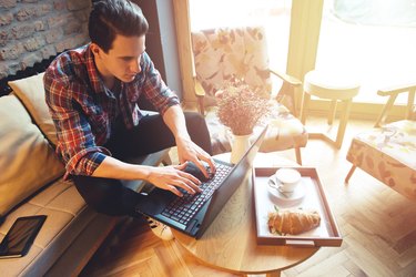 Young man sitting at a cafe, using a laptop, drinking espresso